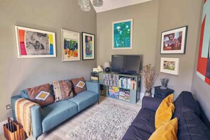 Ein Wohnzimmer mit blauem Sofa, dunklem Sofa, Bücherregal und gerahmten Kunstwerken an den Wänden.