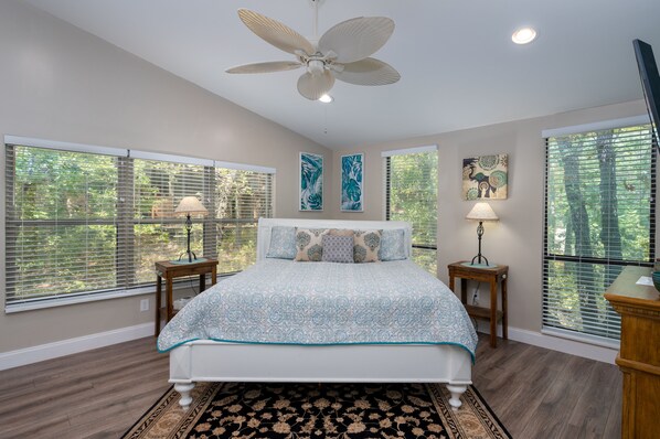 A bedroom with a bed, a ceiling fan, and large windows with blinds.