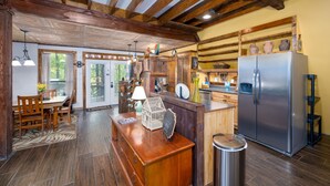 A rustic kitchen with wooden beams, a stainless steel refrigerator, and a dining area with a wooden table and chairs. - Enchanting Lake Texoma Cabin with Hot Tub (Pottsboro)