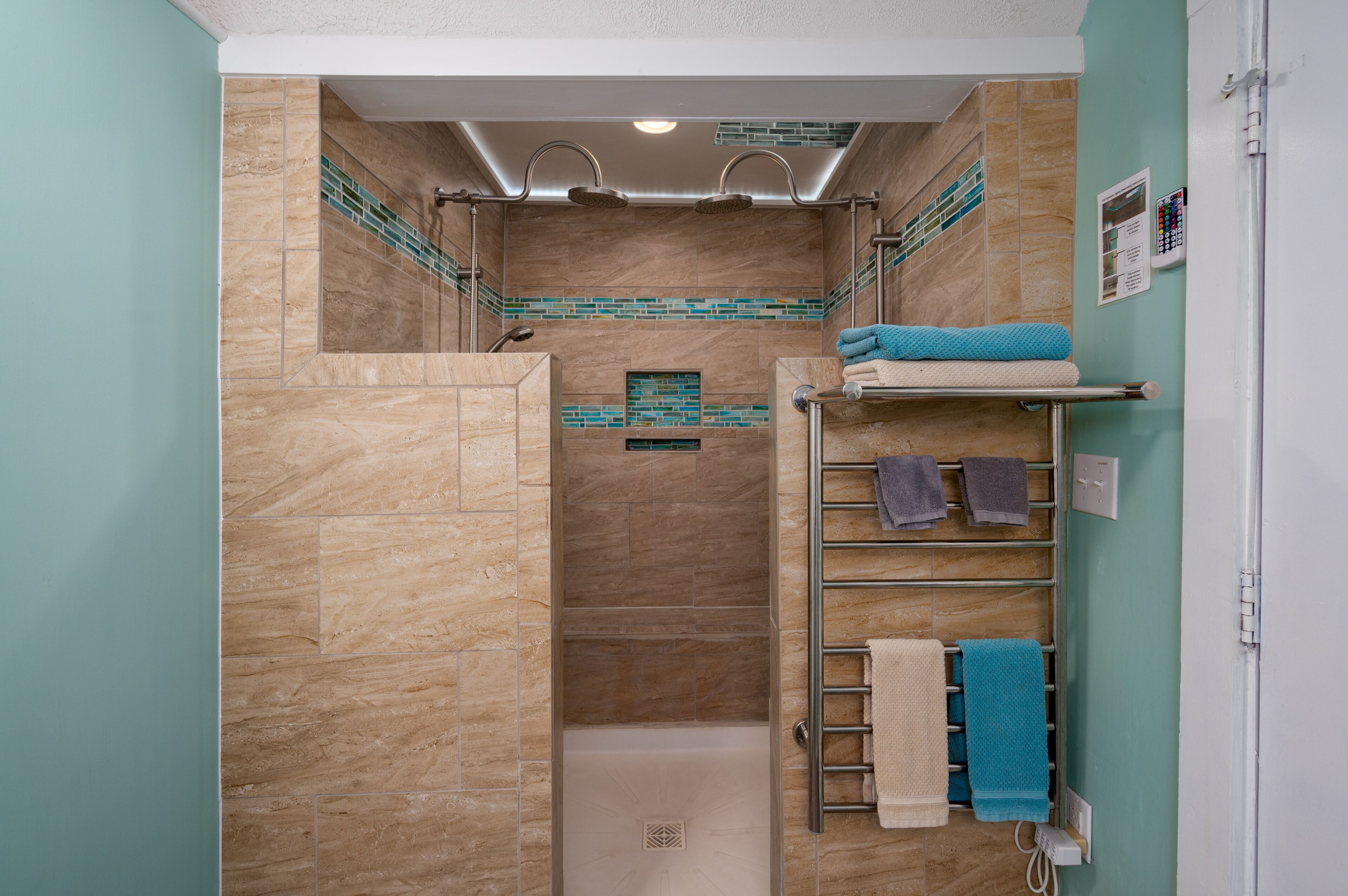 Une douche à l’italienne avec une porte en verre, un porte-serviettes muni de plusieurs serviettes et un mur recouvert de carreaux.