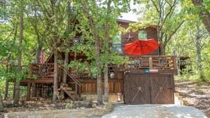A rustic cabin with a wooden deck, a red umbrella, and a stone wall. - Enchanting Lake Texoma Cabin with Hot Tub (Pottsboro)