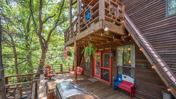 A wooden cabin with a deck, outdoor seating, and a grill. - Enchanting Lake Texoma Cabin with Hot Tub (Pottsboro)