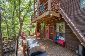 A wooden cabin with a deck, outdoor seating, and a grill.