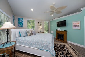 A bedroom with a bed, a ceiling fan, a television, and artwork on the walls.