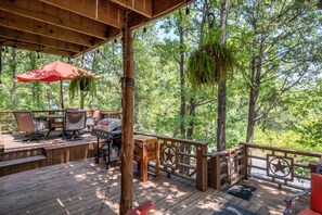 An outdoor deck with wooden furniture, a barbecue grill, and hanging plants.