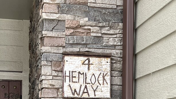 Pareda de pedra com uma placa indicando "4 Hemlock Way" e um grande "A" de madeira fixado nela.