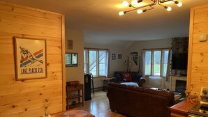 Interior acogedor de una cabaña con paredes de madera, chimenea, comedor y sala de estar con sofá y televisor.