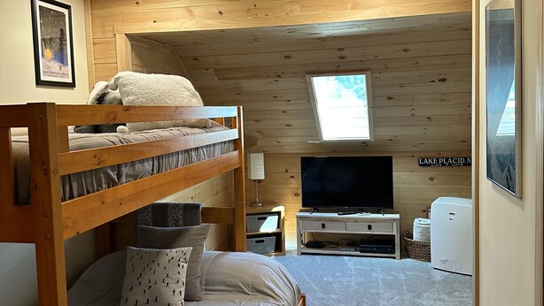 A cozy, well-lit room with a bunk bed, a flat-screen TV, and a refrigerator.