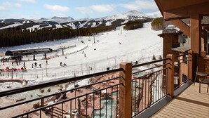Une station de ski dotée d’une terrasse en bois offrant une vue sur une pente enneigée et d’un espace piscine.