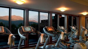 Une salle de sport équipée de tapis de course et d’appareils elliptiques, de grandes fenêtres offrant une vue sur les montagnes et de matériel d’exercice.