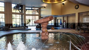 Une grande piscine intérieure dotée d’un rocher central et de plusieurs jets d’eau.