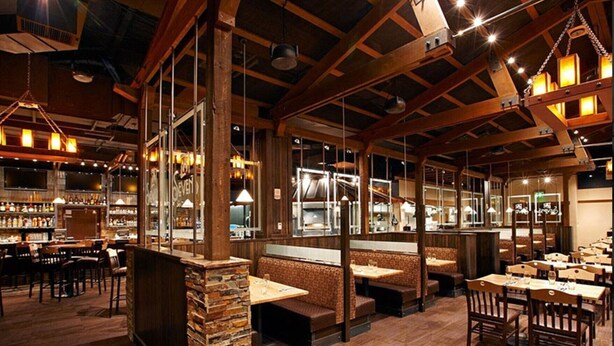 L’intérieur d’un restaurant avec des poutres en bois, des piliers en pierre et un espace bar.