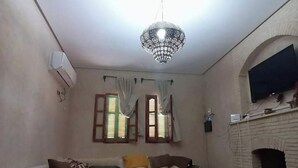 A bedroom with a bed, a chandelier, a fireplace, and two windows with curtains. - JARDIA beautiful vacation villa in the heart of the palm grove (TOZEUR)