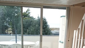 A covered patio with a table and chairs, a sliding glass door, and a view of the outdoors. - Apartment with sea view 100m from the beach 2* (2*) (Saint-Gildas-de-Rhuys)