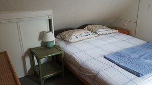 A bedroom with a bed, pillows, a lamp, a nightstand, and a small table. - Apartment with sea view 100m from the beach 2* (2*) (Saint-Gildas-de-Rhuys)
