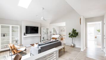 Un salon spacieux comprenant un canapé, des fauteuils, un téléviseur et un ventilateur de plafond.