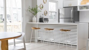 A modern kitchen with white cabinetry, a stainless steel refrigerator, a built-in oven, and a small island with stools. - Serene home with all the comforts of a fully designed space- 3 🛏/2 🛁 House (Chesterfield)