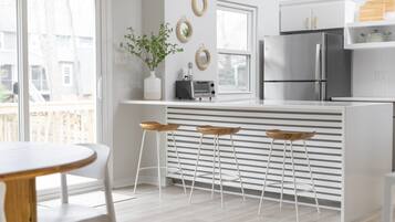 Une cuisine moderne avec des meubles blancs, un réfrigérateur en acier inoxydable, un four encastré et un petit îlot central avec des tabourets.