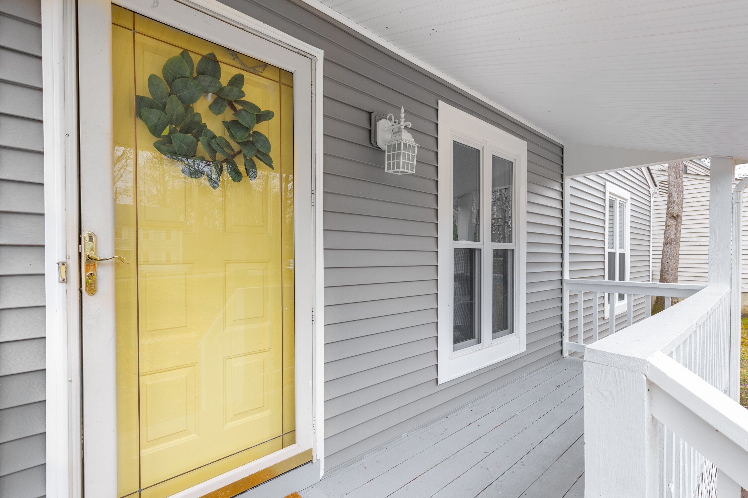 Une maison avec une porte d’entrée jaune, des volets blancs et une balustrade de porche blanche.