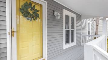 Une maison avec une porte d’entrée jaune, des volets blancs et une balustrade de porche blanche.