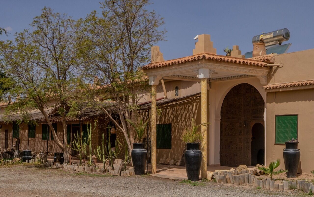 A traditional building with a courtyard, featuring a large arched doorway, a covered patio area, and potted plants.