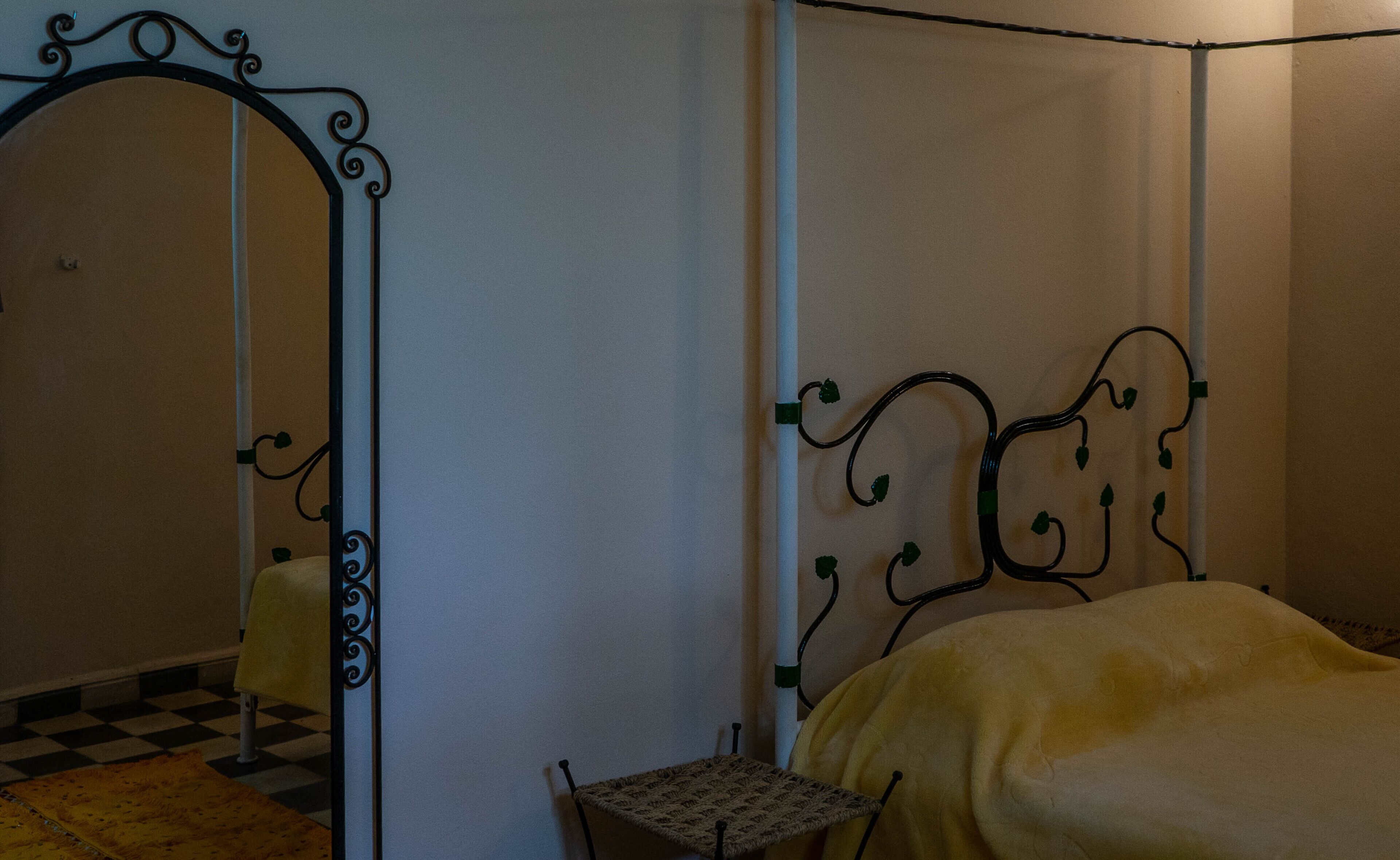 Una habitación con cama, una mesita pequeña y un espejo con marco decorativo.