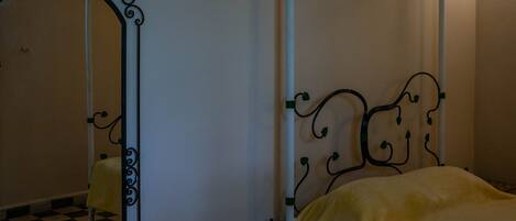 Una habitación con cama, una mesita pequeña y un espejo con marco decorativo.