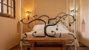 Un lit à baldaquin orné de motifs d’arbres, une tête de lit en bois et une table ronde en bois placée devant.