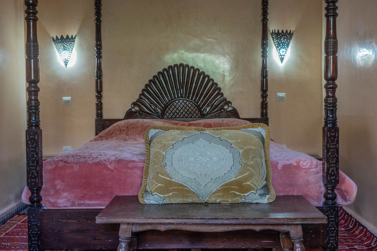 A four-poster bed with a decorative headboard, a plush red bedspread, and a patterned pillow.