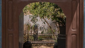 Un portail en arc donne accès à une cour intérieure dotée d’un sol carrelé, d’un grand bac à plantes et d’une clôture décorative.