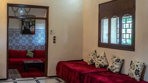 Une pièce avec un canapé rouge, un lit recouvert de velours rouge et un mur orné d’un motif.
