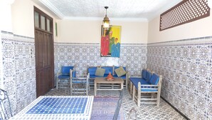 Une pièce aux murs recouverts de carreaux décoratifs, une porte en bois, un canapé bleu, une petite table avec une théière et un luminaire suspendu.