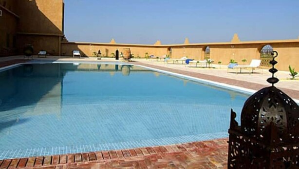 Une piscine dont le bord est recouvert de carreaux, bordée de briques, et ornée d’un élément décoratif en métal sur le côté droit.