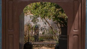 Un portail en arc donne accès à une cour intérieure dotée d’un sol carrelé, d’un grand bac à plantes et d’une clôture décorative.