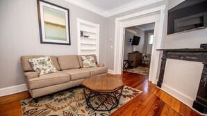 Een woonkamer met een beige bank, gekleurde kussens, een houten salontafel en een decoratief vloerkleed.