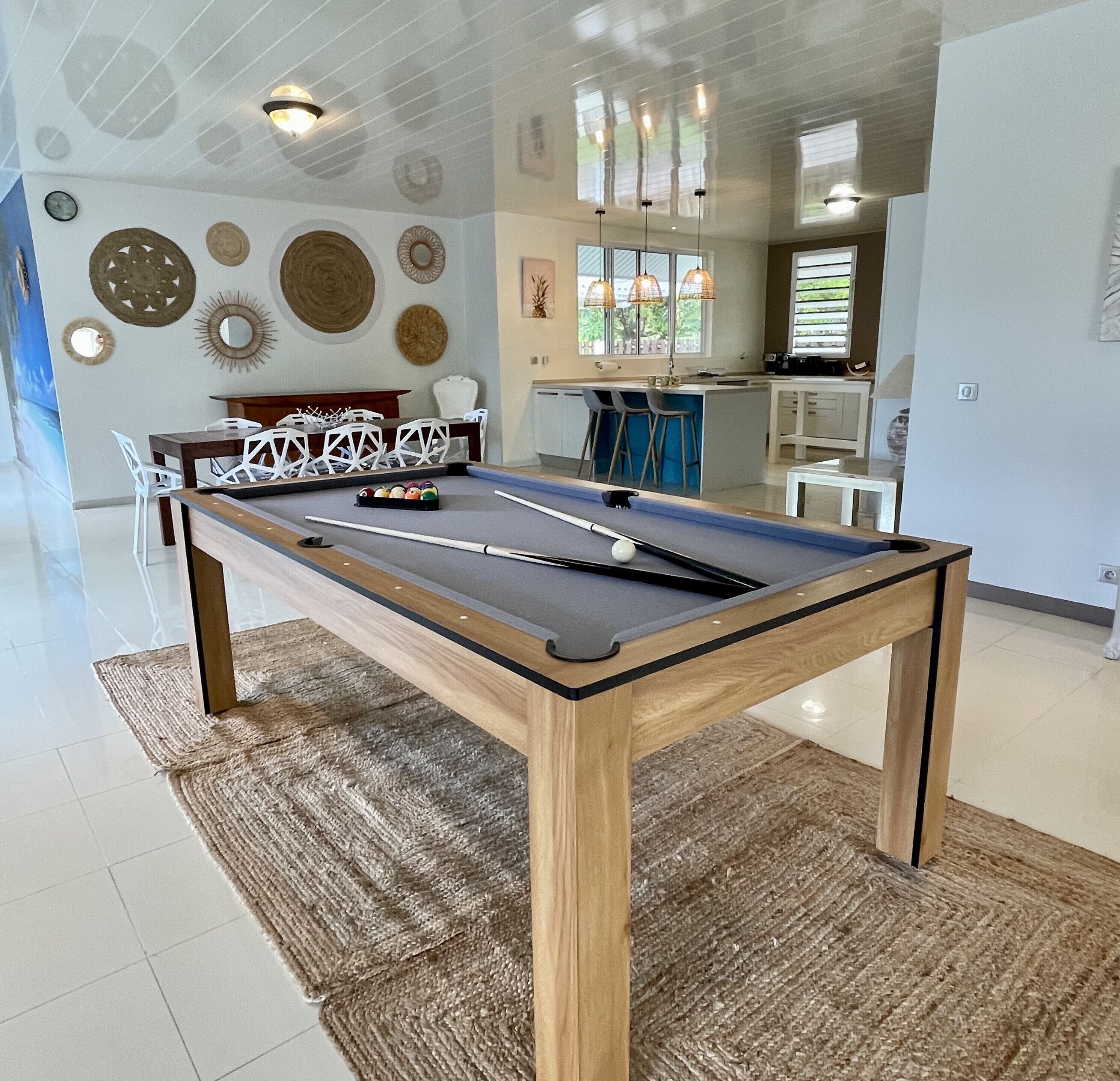 A pool table with a wooden frame and a dark felt surface, surrounded by a woven rug.