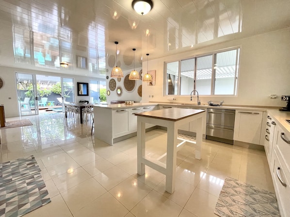 A spacious kitchen with a central island, large windows, and modern pendant lighting.