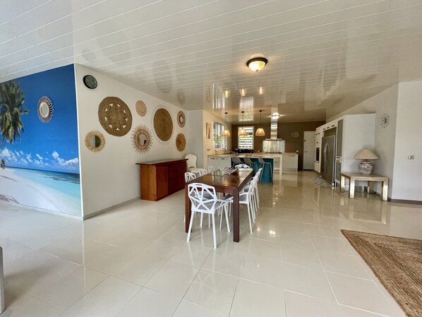 A spacious kitchen with modern appliances, a dining area with white chairs, and a large decorative wall mural.