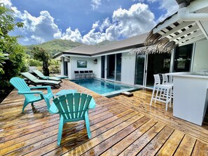 A poolside area with a wooden deck, lounge chairs, and a bar area.