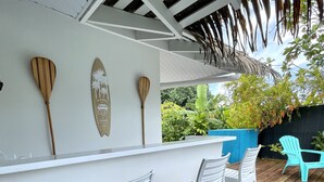 Una terraza de madera con sillas de plástico blanco y una barra blanca.
