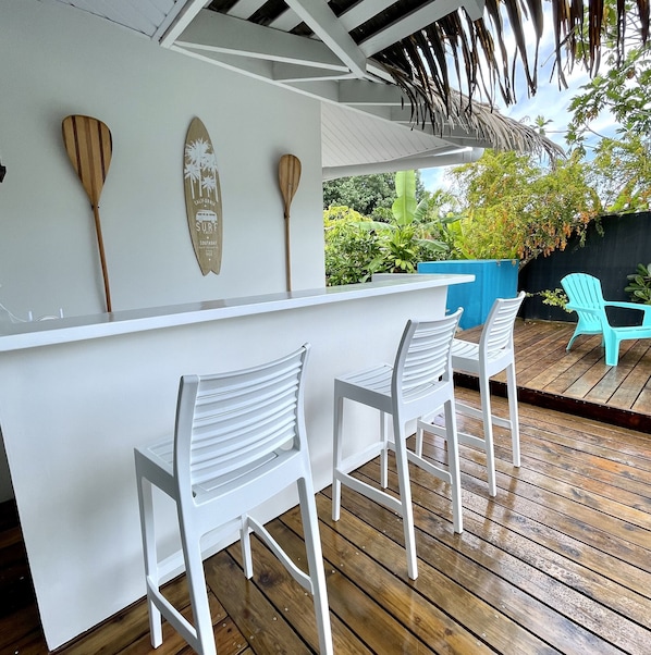 A wooden deck with white plastic chairs and a white bar counter.