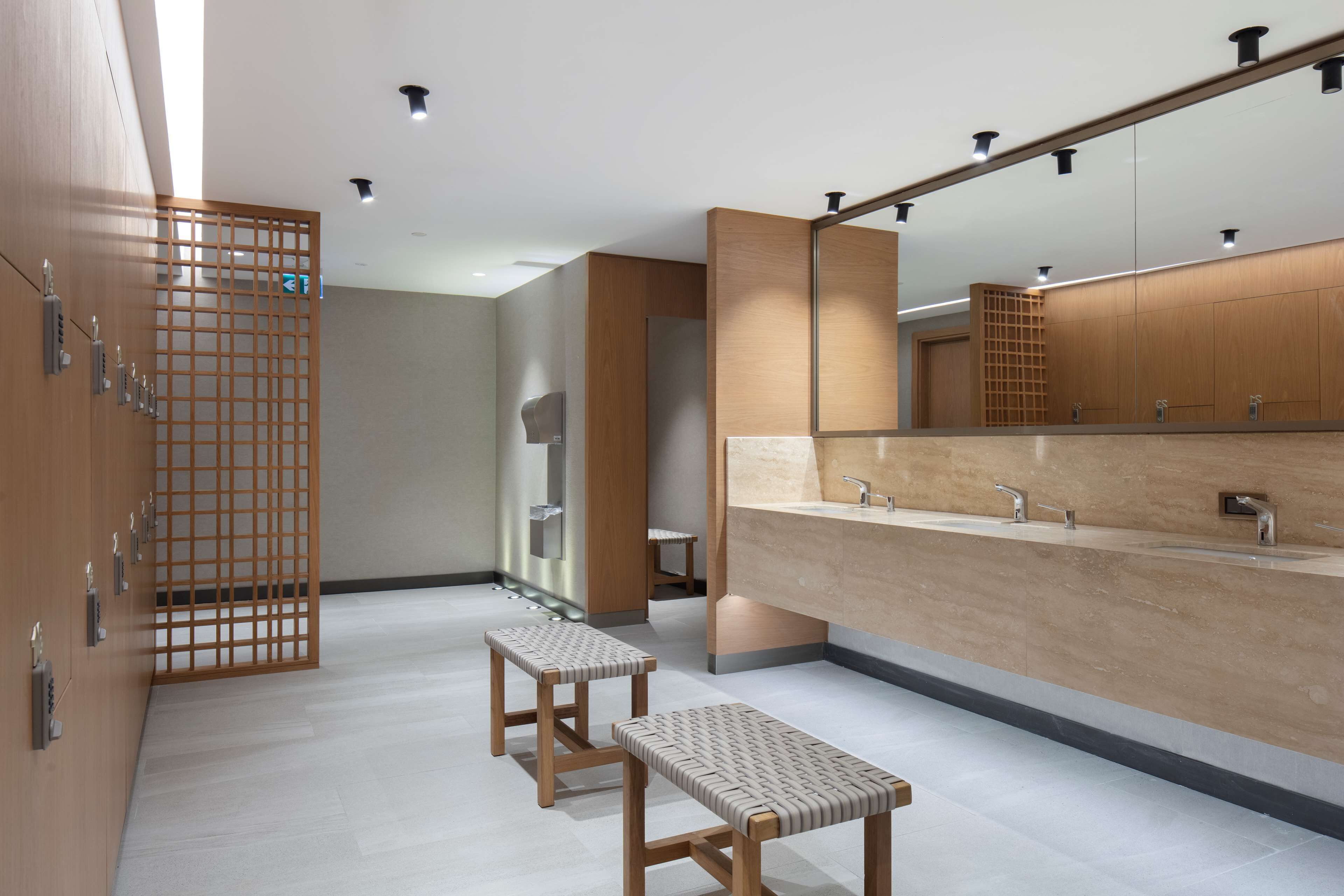 Un baño moderno con un espejo grande, armarios de madera y dos taburetes.