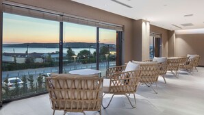 Un balcón con sillas de mimbre y una mesa, con vistas a la costa y un puerto deportivo.