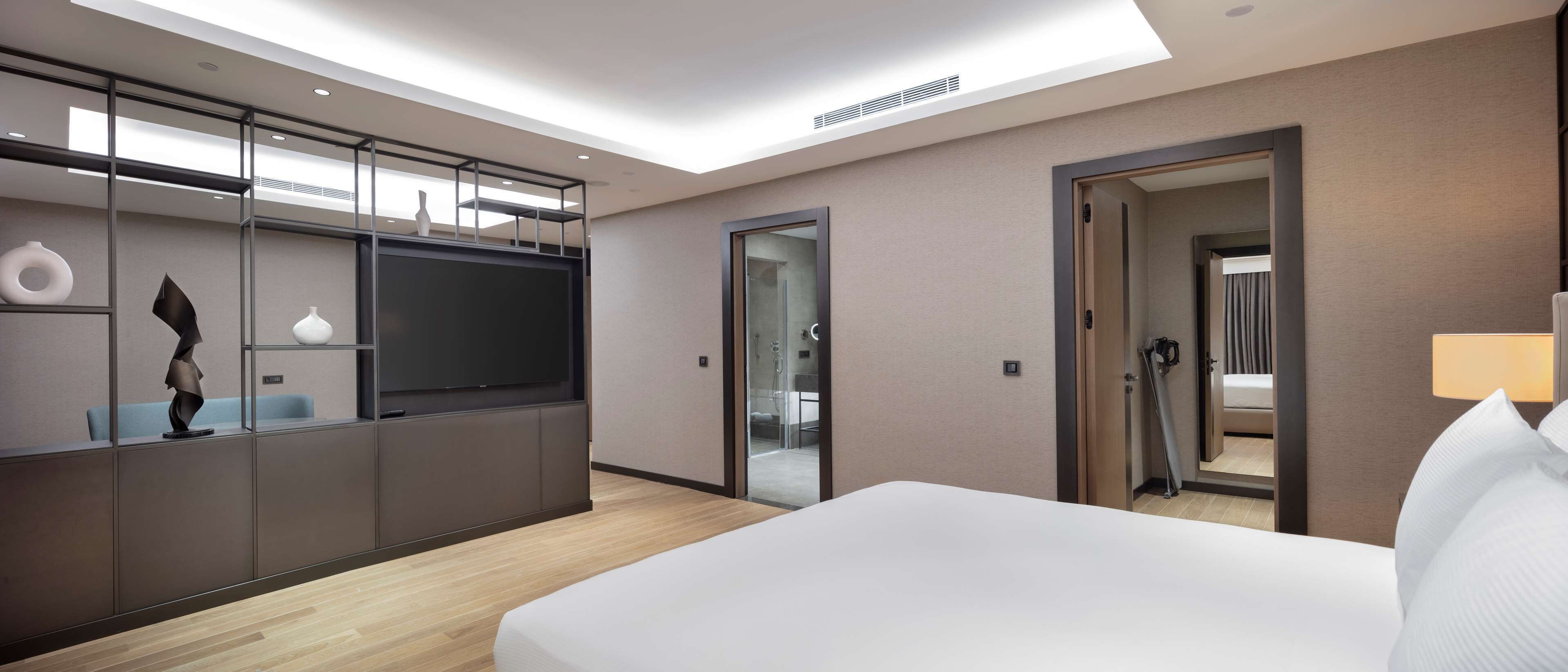 Een moderne hotelkamer met een groot bed, een televisie, een bureau met stoel, en een badkamer zichtbaar door een glazen deur.