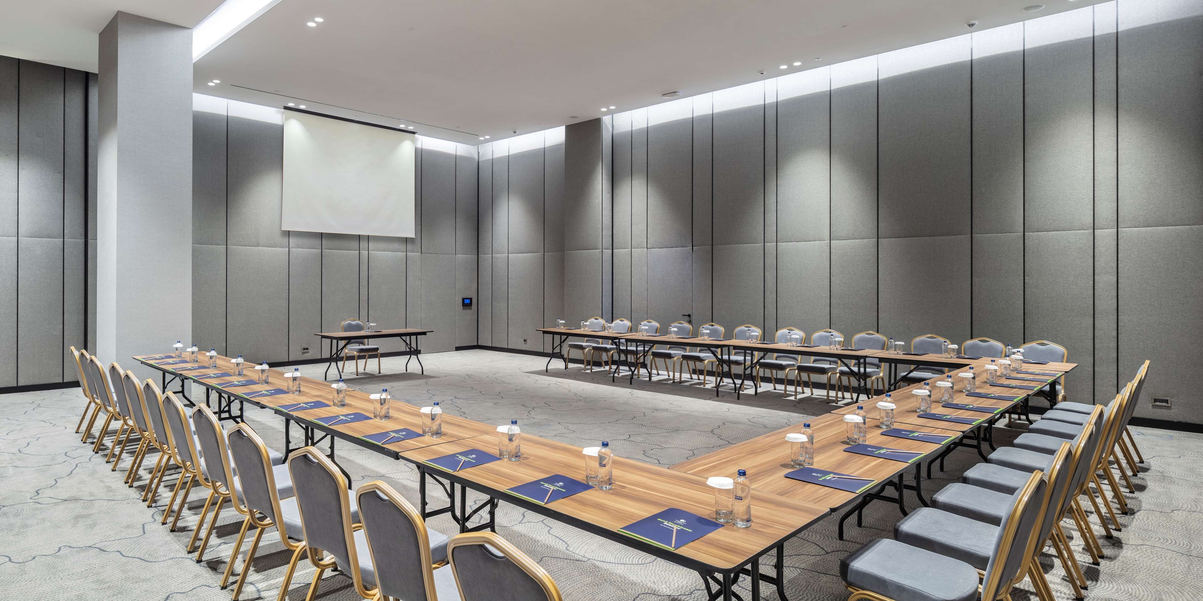 A conference room with long tables, chairs, and a projector screen.