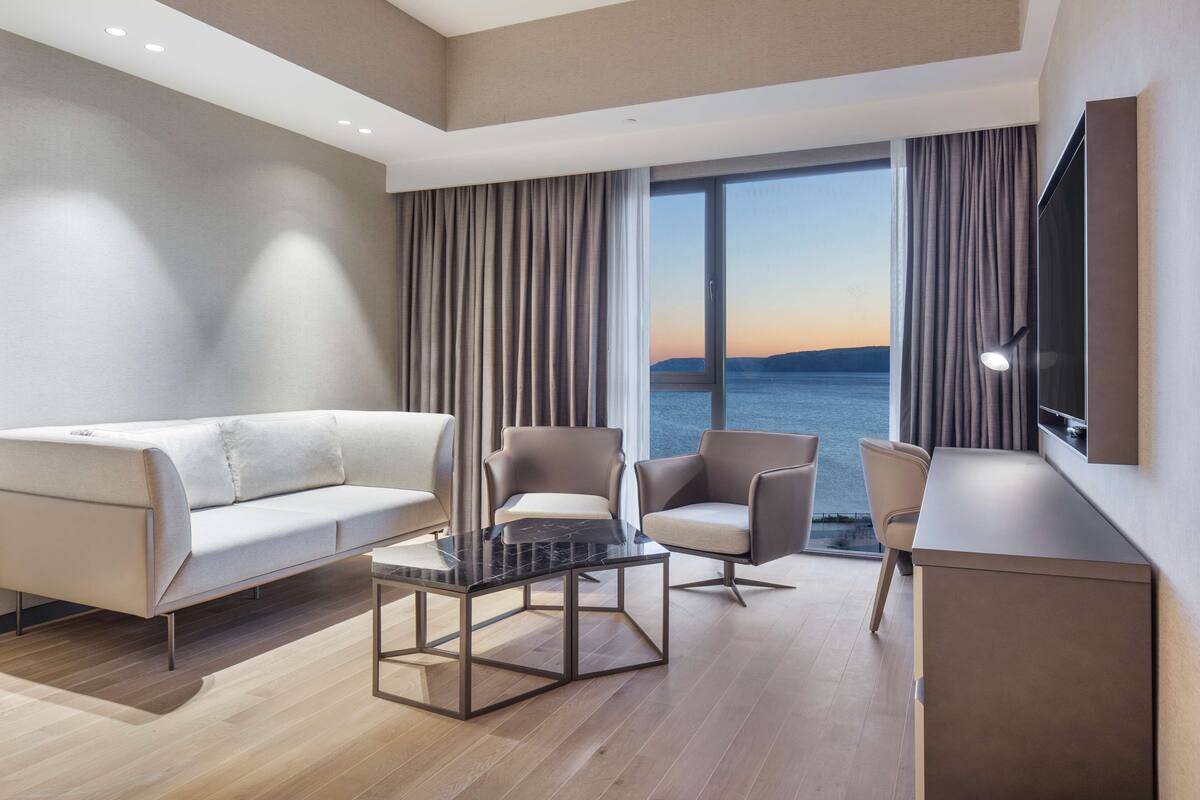 A modern hotel room with a sofa, chairs, a coffee table, and a TV.