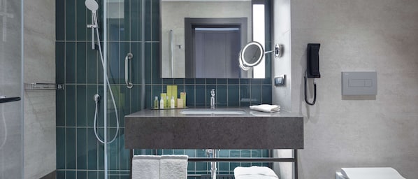 A modern bathroom with a shower, a sink with toiletries, a mirror, and a phone.