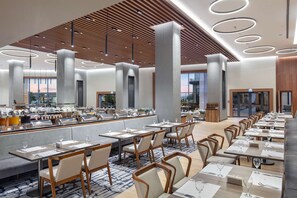 Enjoy meals in our dining area, featuring multiple tables and chairs, a buffet, and large windows offering views of the surrounding area.