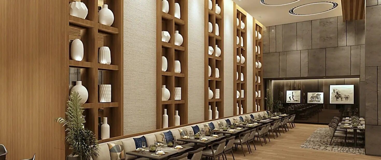 Una larga mesa de comedor con sillas, rodeada de estanterías de madera con jarrones blancos.