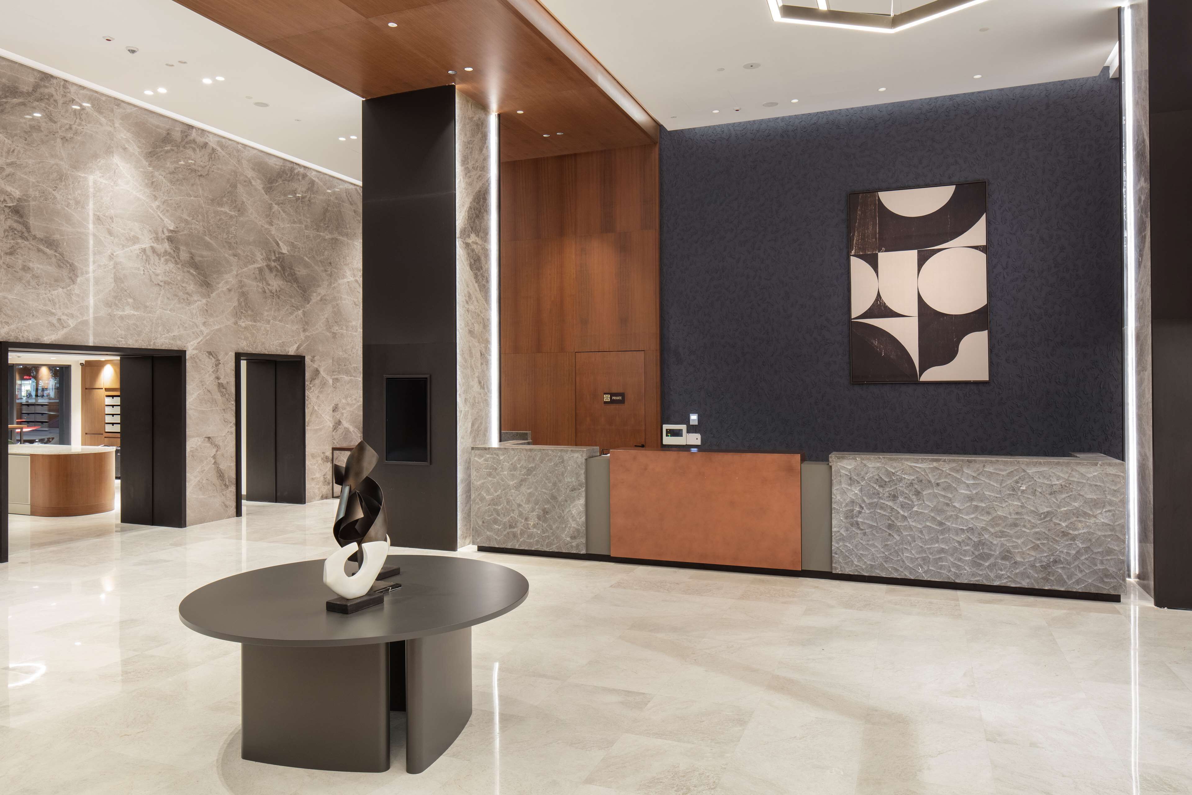 Een moderne lobby met een marmeren vloer, een receptiebalie en een groot abstract kunstwerk aan de muur.